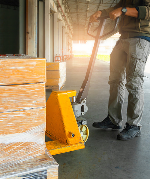 a person moving a pallet of stack boxes using a pallet jack